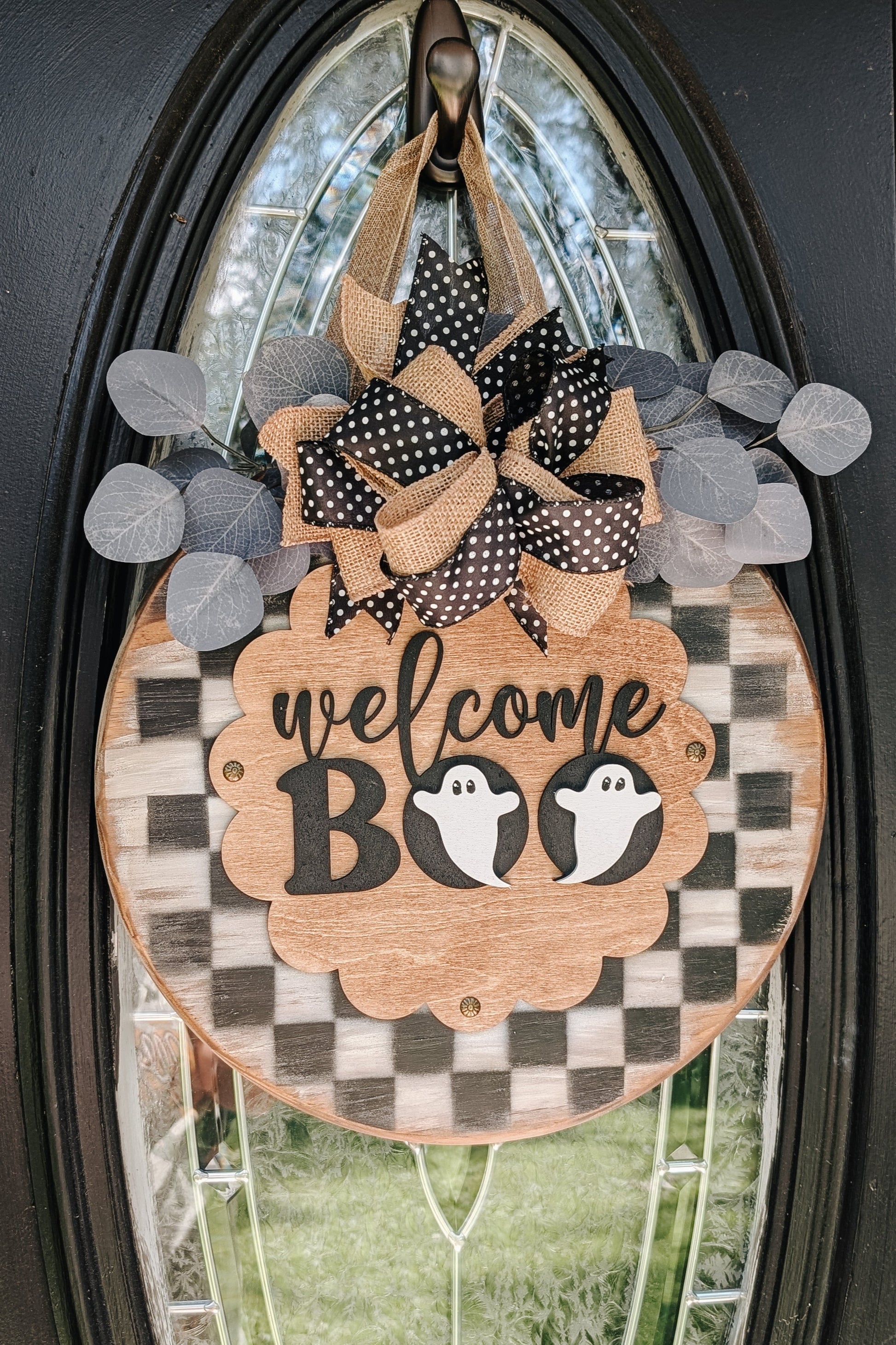 Decorative Halloween door hanger with 'welcome BOO' text and ghost designs on a glass door.